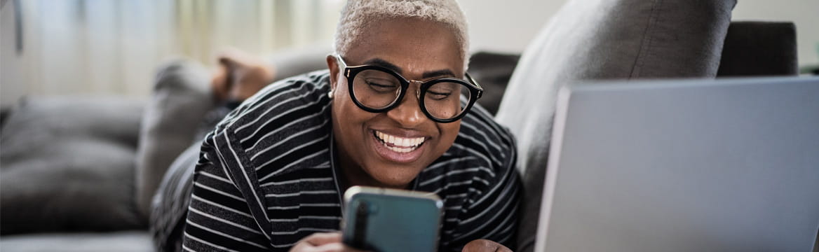 vrouw ligt op de bank met mobiel en laptop
