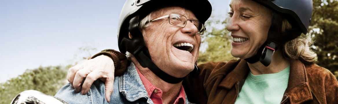 oudere man zit op scooter en jonge vrouw staat bij hem terwijl ze lachen