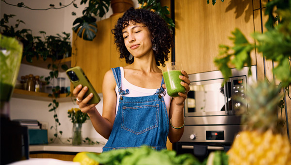 Vrouw in keuken met telefoon en een smoothie