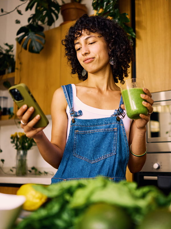 Vrouw in keuken met telefoon en een smoothie